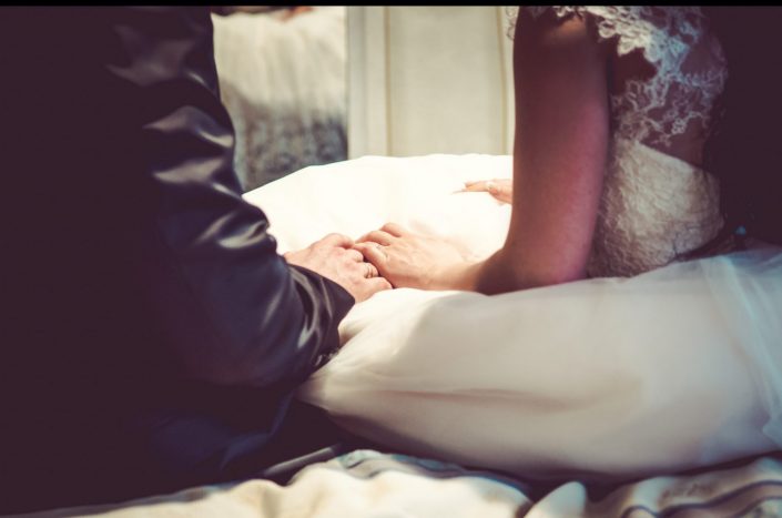 Ein Hochzeitspaar erlebt seinen schönsten Tag noch ein Mal bei einem Afterweddingshooting und Hält seine Hände auf einem Bett