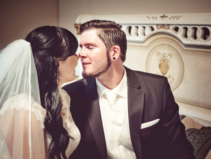 Ein Hochzeitspaar erlebt seinen schönesten Tag noch ein mal und küsst in einem Hotelzimmer im Ein Hochzeitspaar kuschelt auf einem Bett im Häckers Grand Hotel Bad Ems